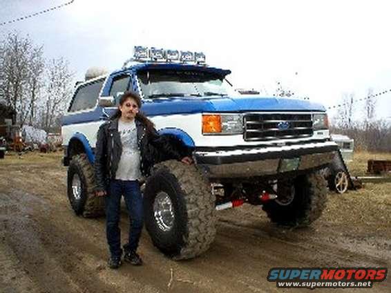 Person standing next to a lifted Ford Bronco with large tires and light bar