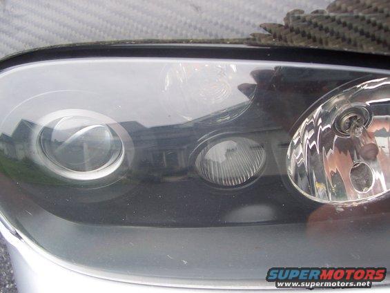 Close-up of a car headlight assembly with multiple bulbs and a carbon fiber trim piece above
