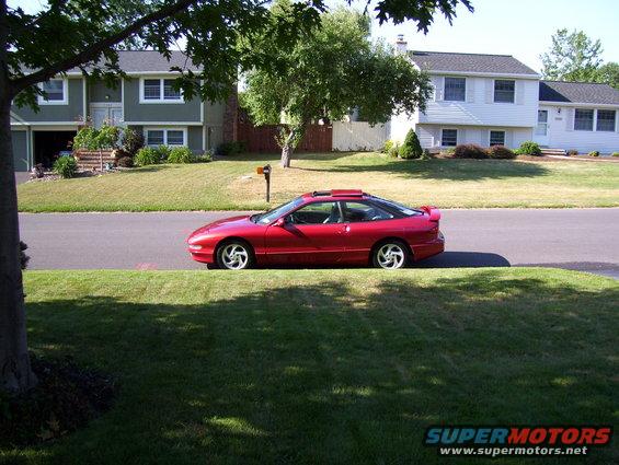 Red coupe parked on street, side view. Sunroof and spoiler visible