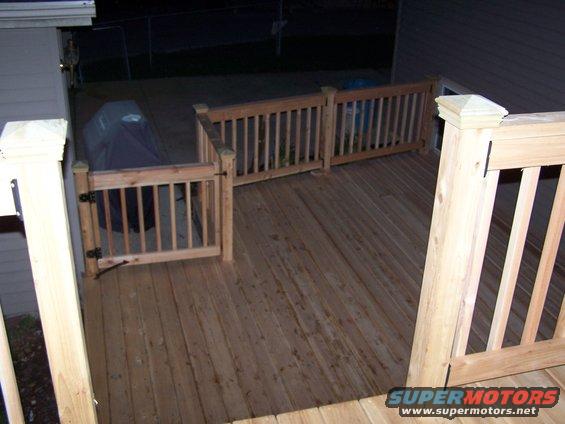 Wooden deck with a covered grill and railings. A "SUPERMOTORS" watermark is visible