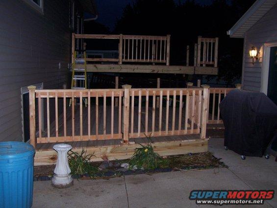 Newly built wooden deck with railings, a ladder, and a blue trash can