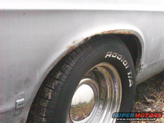 Close-up of a car's rear wheel well showing rust and a Radial T/A tire on a chrome rim