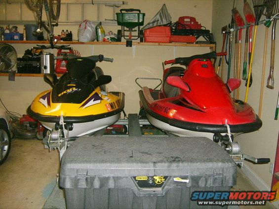 Two jet skis, one yellow and one red, parked in a garage