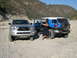 2007 Toyota FJ Cruiser - A silver Toyota Tacoma and a blue 2007 Toyota FJ Cruiser are parked in a rocky, dry riverbed with mountains in the background.