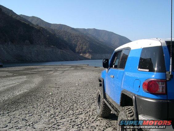 Blue 2007 Toyota FJ Cruiser with white roof parked on a dry, sandy shore next to a body of water