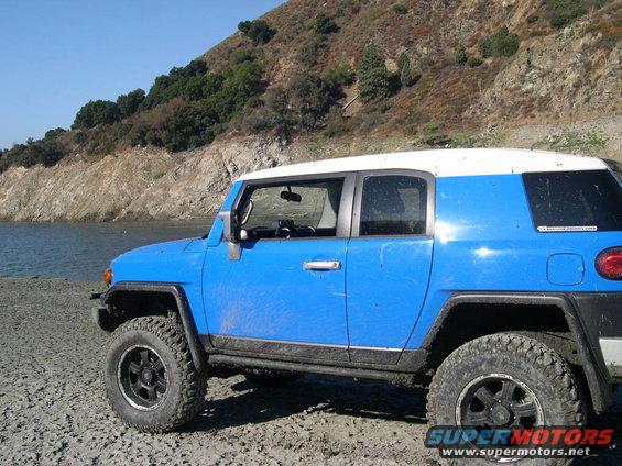 Blue 2007 Toyota FJ Cruiser with white roof parked on a dirt shore next to water