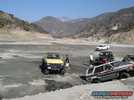 Yellow Toyota pickup truck stuck in mud with other off-road vehicles
