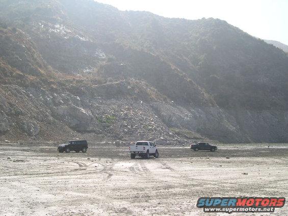 three SUVs and trucks driving on a dry, rocky terrain with a large hill in the background