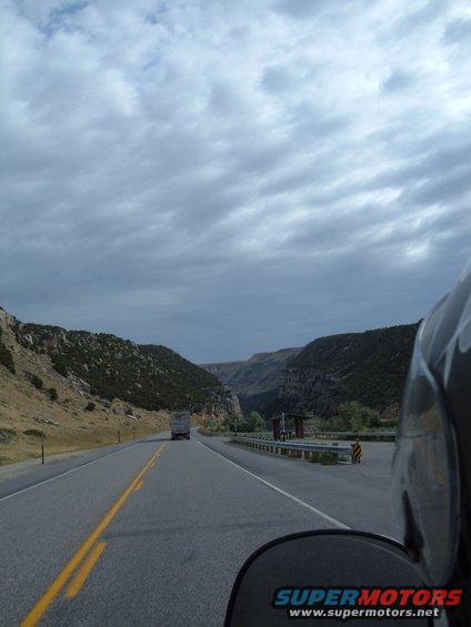 Motorcycle rider's view of a highway with a truck ahead, passing through a canyon