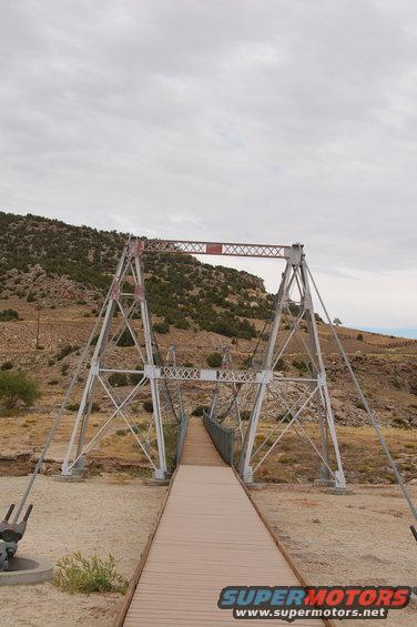 Suspension bridge with wooden walkway over dry creek bed, rocky hills in background