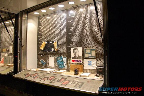 Display case with a wall of names, a portrait of a man labeled "HAGEL", and various items on shelves