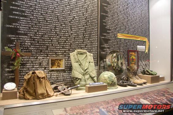 Display case with Vietnam Veterans Memorial wall, military uniform, helmet, boots, and backpack