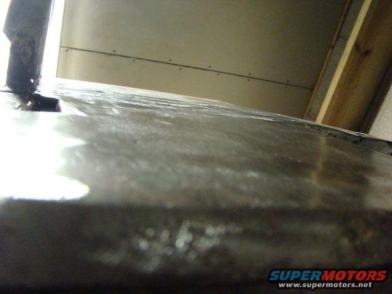 Close-up of a dull metal panel with water spots, showing a vertical support on the left and a wall in the background