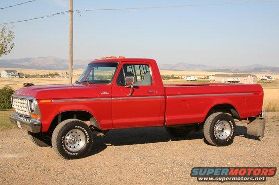 Red 1979 Ford F-150 pickup truck, side view, parked on a dirt road with houses and hills in the background