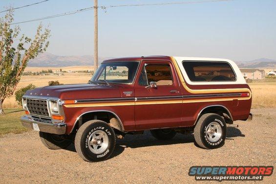 Maroon Ford Bronco with white top and gold stripe detail, parked on a dirt road
