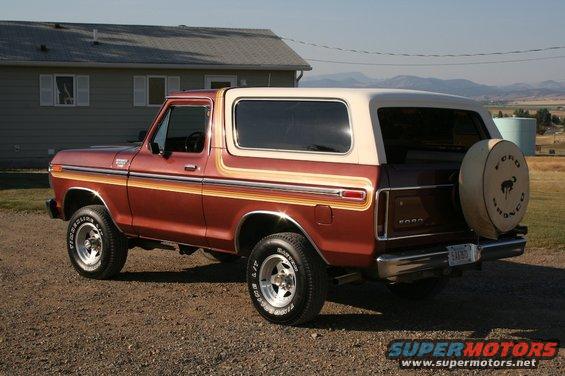 Red 1978 Ford Bronco with tan top and side stripes, spare tire on rear, parked on gravel