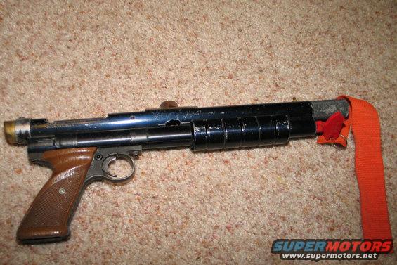 Air gun with brown grip and orange strap attached to the barrel