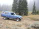 2006 Ford E350 - A blue pickup truck with a camper shell is parked on a dirt road surrounded by trees and fog.