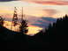 2006 Ford E350 - A vibrant sunset paints the sky with hues of orange, pink, and purple above a dark, forested mountain landscape.