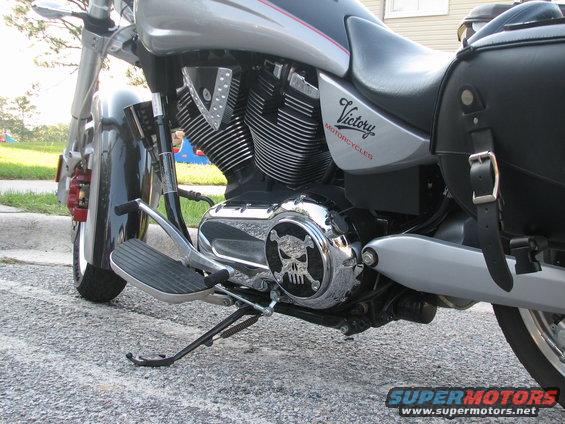 Silver motorcycle engine with a skull emblem on the cover and a black saddlebag