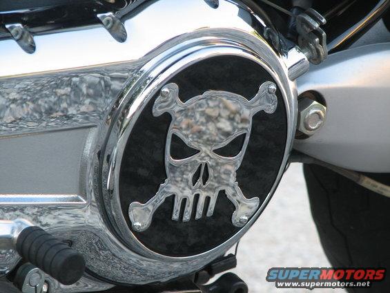 Close-up of a motorcycle engine cover with a chrome skull and crossbones emblem on a black background