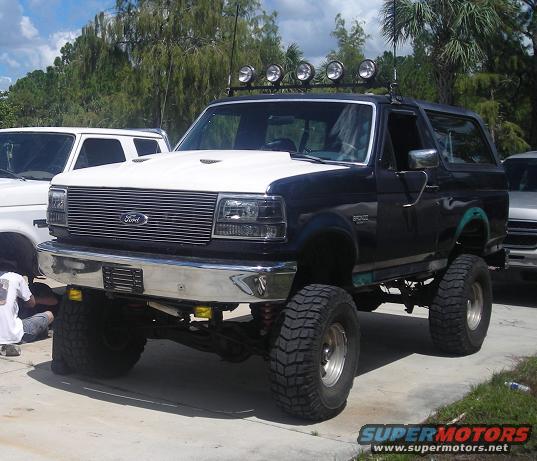 Black and white Ford Bronco with off-road tires and light bar, parked on concrete
