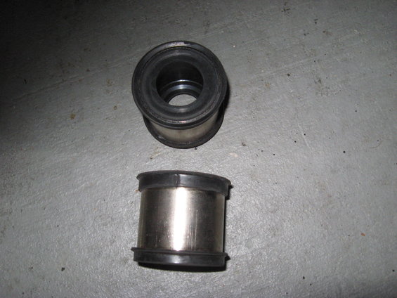 Two metal and rubber bushings on a gray concrete surface