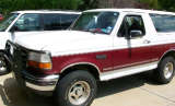Two-tone white and maroon Ford Bronco parked next to a white van