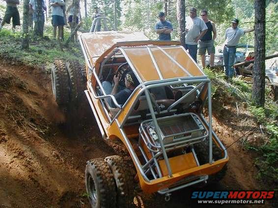 Orange off-road buggy with a roll cage climbing a dirt hill, driver visible