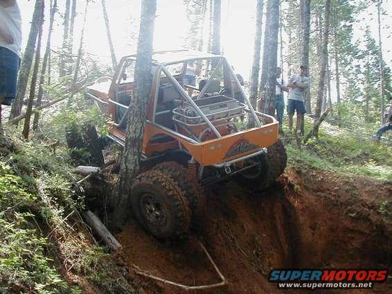 Orange off-road vehicle with roll cage climbing steep dirt embankment