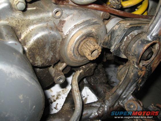 Close-up of a dirty, splined shaft protruding from a motorcycle engine casing