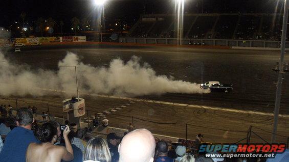 Car doing a burnout on a track at night, kicking up a lot of smoke