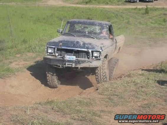 Muddy pickup truck driving through dirt and grass, kicking up dust. License plate reads ZJO382