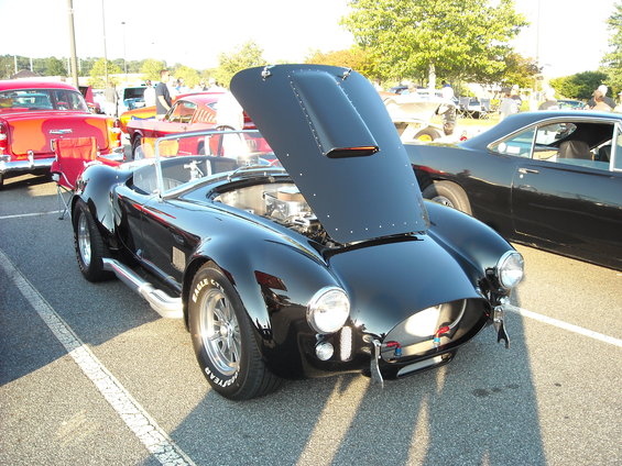 Black AC Cobra replica with hood open, side pipes, and racing tires