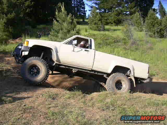 White pickup truck with large tires driving off-road, front bumper visible
