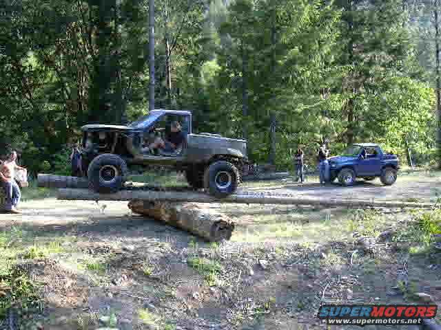 Gray pickup truck on logs, blue Suzuki Samurai nearby