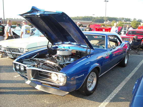 Blue muscle car with hood open at a car show. Another red car is visible