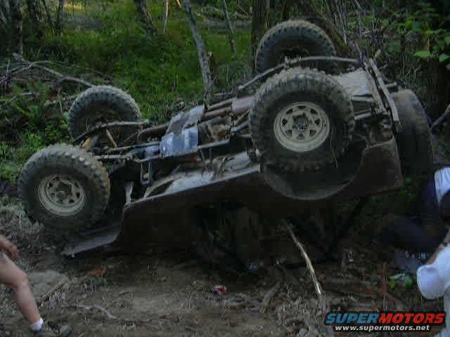 Off-road vehicle flipped onto its side in a wooded area. Tires and undercarriage are visible