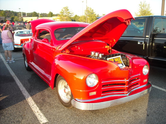 Red coupe with hood open, showing engine and a "For Sale" sign. Chrome bumper and grille visible