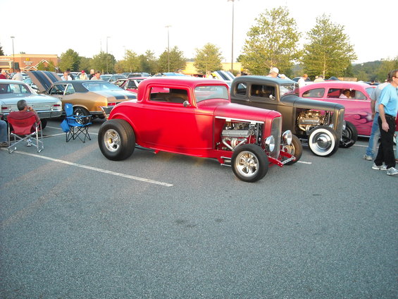 Red hot rod coupe with exposed engine, parked next to other custom cars