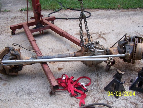 Vehicle axle assembly suspended by chains from an engine hoist, with jack stands nearby