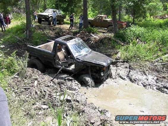 Black pickup truck stuck in a mud pit, another truck and people in the background