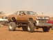 1992 Ford Bronco - A heavily modified coupe with oversized tires and dual exhaust stacks sits on a trailer in a dirt lot.