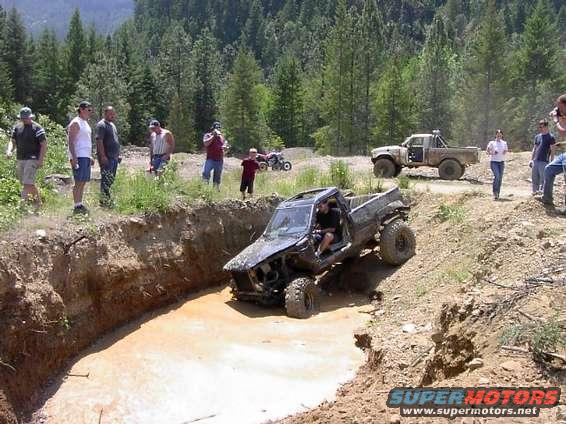 Mud-covered pickup truck with open doors descending into a muddy pit