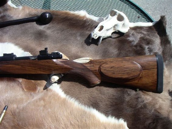 Rifle with wooden stock and scope, laid on animal hide next to a skull