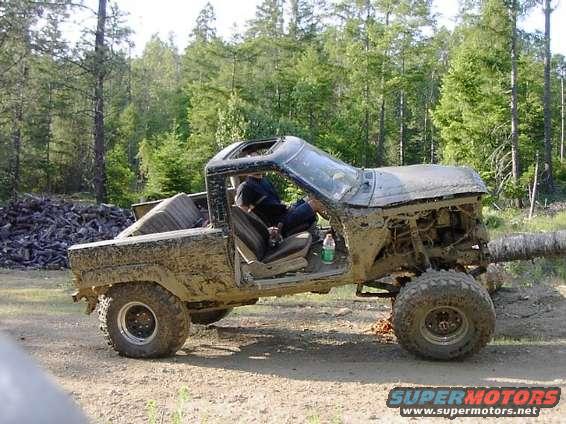 Mud-covered off-road vehicle with open roof and doors, parked on a dirt path