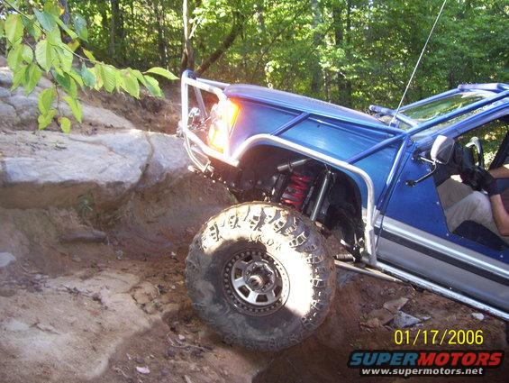 Blue off-road vehicle with roll cage climbing over rocks on a dirt trail