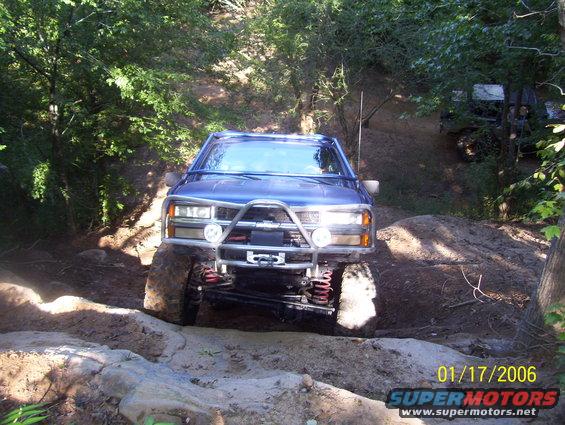 Blue pickup truck with a winch and brush guard navigating a rocky trail