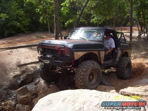1978 Ford Bronco modified for off-roading, driving over rocks. Driver visible inside