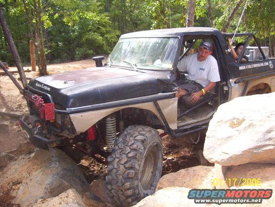 Modified pickup truck with large tires navigating rocks, driver in seat